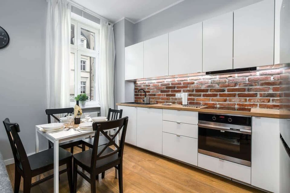 A modern kitchen area with white cabinets, a dining table, and brick backsplash, partly open to the living room.