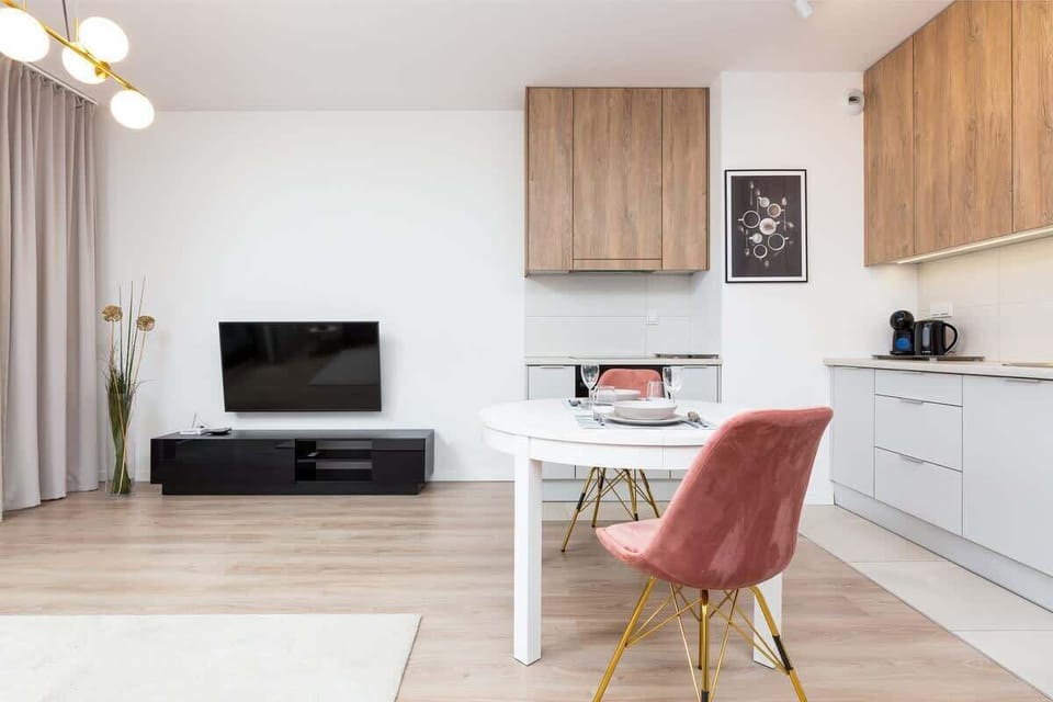 The bright living room with kitchenette creates a functional space, A flat-screen TV hangs on one of the walls.