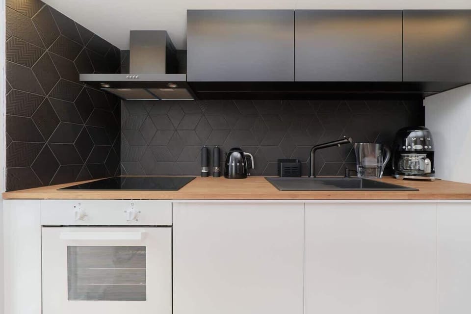 A modern kitchen featuring white cabinets, a black backsplash, and built-in appliances like a oven.
