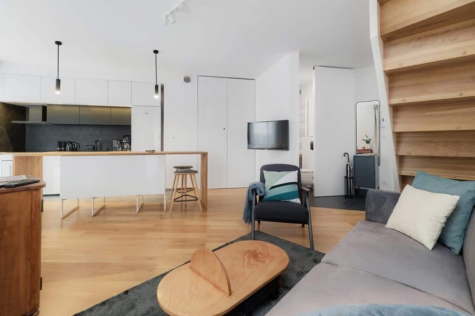 View from the grey sofa to the kitchenette with white and black furniture. The kitchen island harmoniously connects the living and kitchen area. 