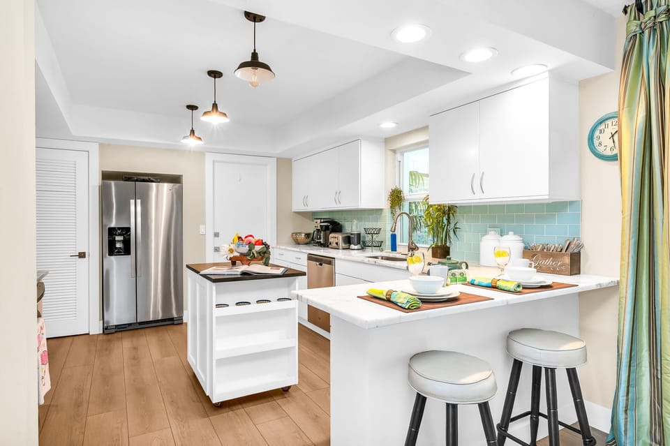 The impressive kitchen is complete with stainless steel appliances and double stainless fridge, a gorgeous aqua tile backsplash, white elegant cabinets, and an island for additonal cooking preparation.