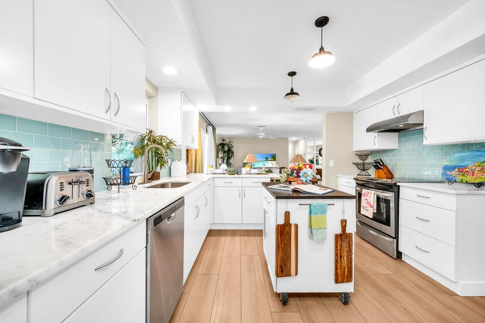 The impressive kitchen is complete with stainless steel appliances and double stainless fridge, a gorgeous aqua tile backsplash, white elegant cabinets, and an island for additonal cooking preparation.