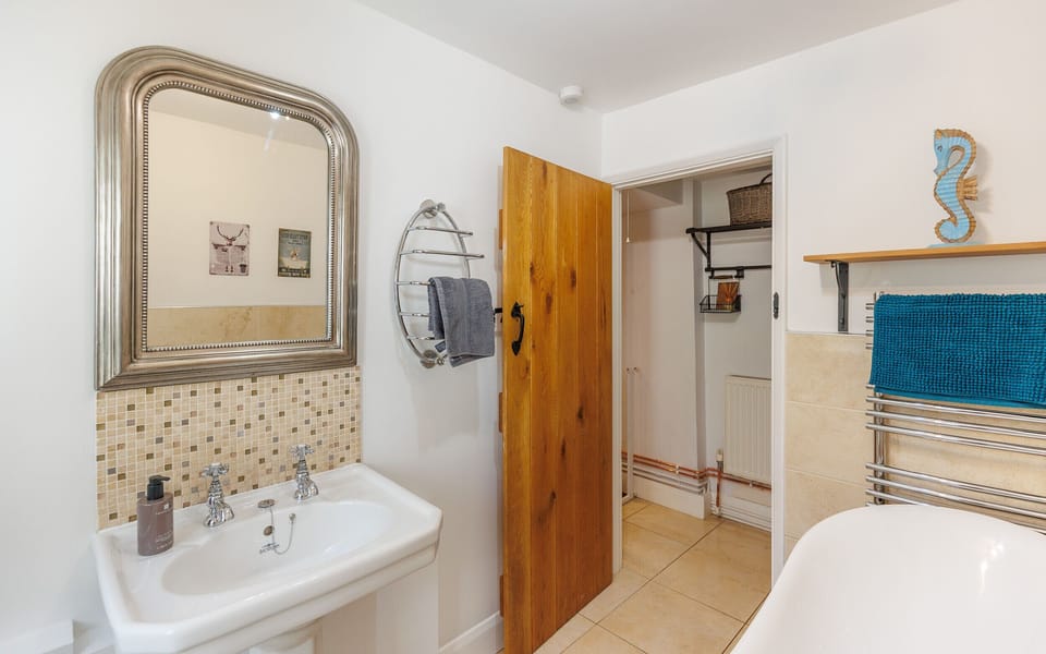 The stylish downstairs family bathroom at 1 Apse Castle Cottages features a freestanding roll-top bath, wash basin, toilet and heated towel rail. A comfortable space to relax and unwind during summer holidays on the Isle of Wight.