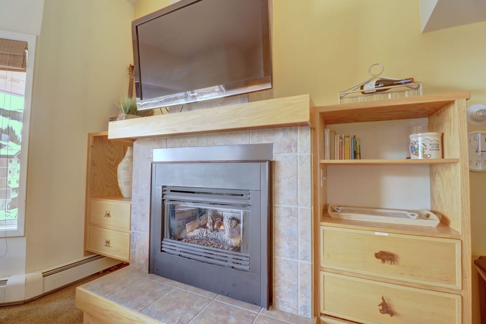 Living room fireplace with a mounted TV above it, flanked by wooden cabinets on both sides. The fireplace has a tiled surround and a tile hearth. The right cabinet has books and decor.