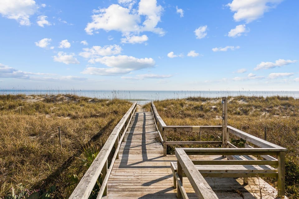 Wooden boardwalk leads through coastal dunes to pristine beach access with ocean views beyond.