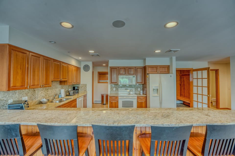 The fully stocked kitchen features warm wood cabinetry, modern appliances, and a large breakfast bar with seating for six