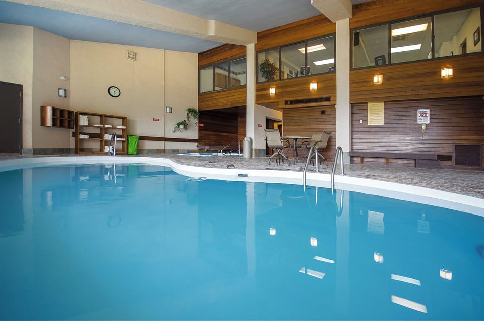 An inviting indoor pool surrounded by warm wood accents, with poolside seating and upper-level viewing areas for a relaxing swim experience.