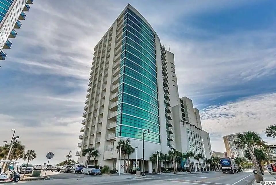 Modern high-rise with sleek glass design above a lively coastal street scene.