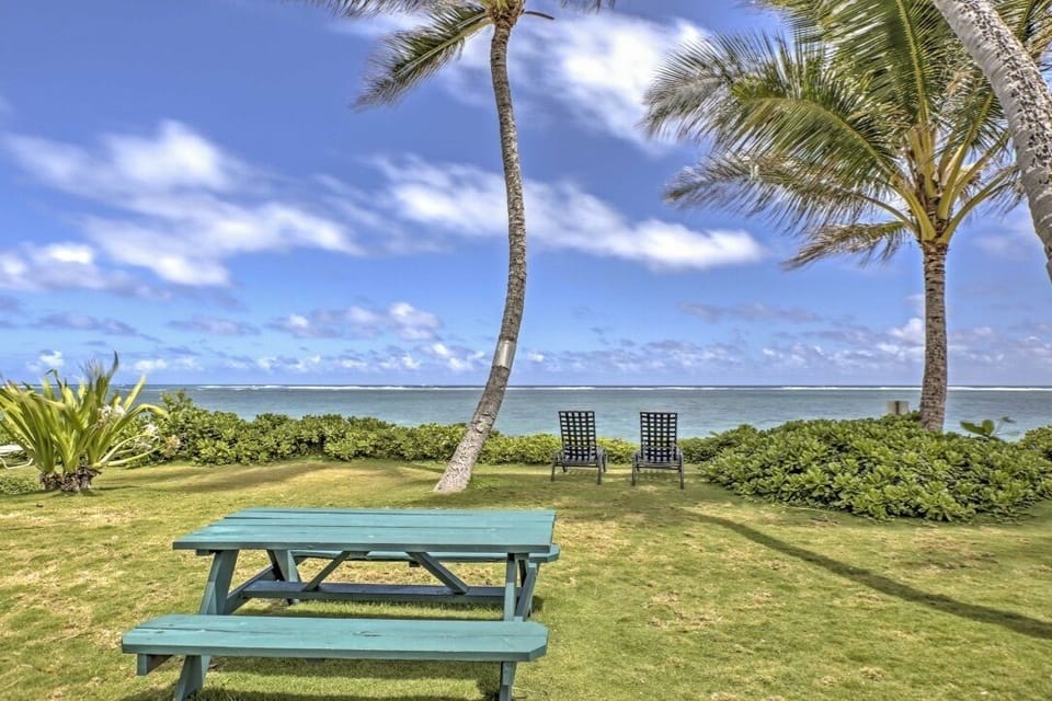 Picnic tables + lounge chairs in front of the cottages, facing the sandy beach.