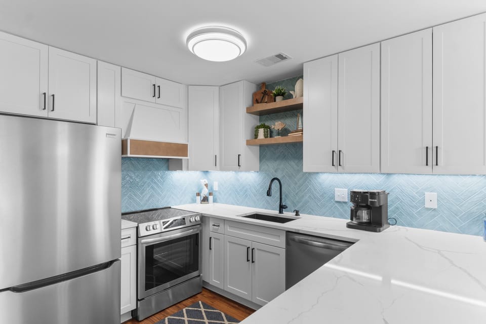 Your fully equipped kitchen features sleek white cabinets, stainless steel appliances, and a stunning blue herringbone backsplash that adds coastal charm to your cooking space.