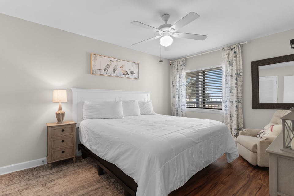 Sink into crisp white linens in your serene bedroom, where coastal artwork and gentle ceiling fan create the perfect sleep sanctuary.