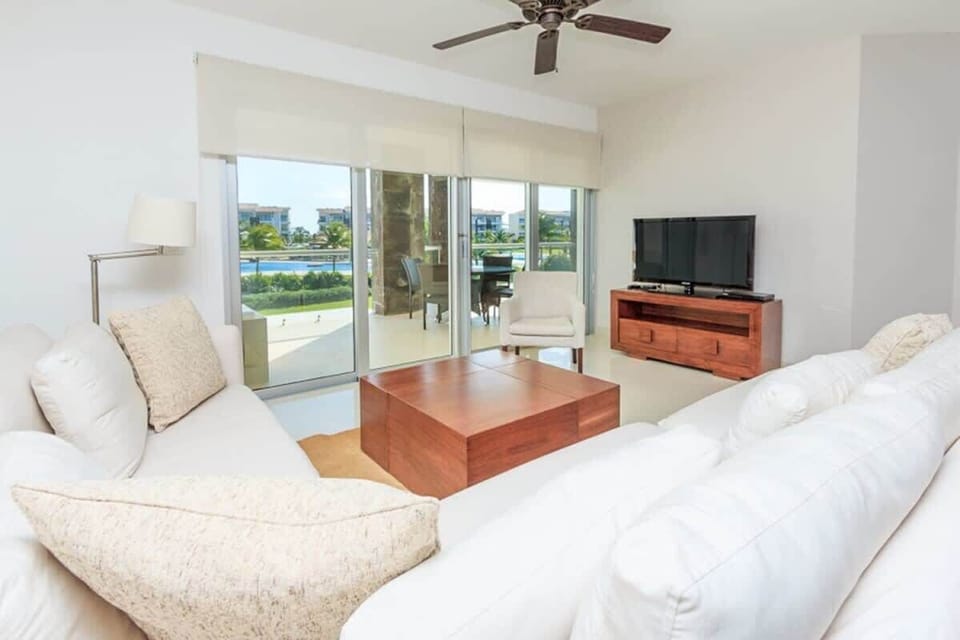 Bright living room with white sofas and a view of the pool through sliding glass doors.