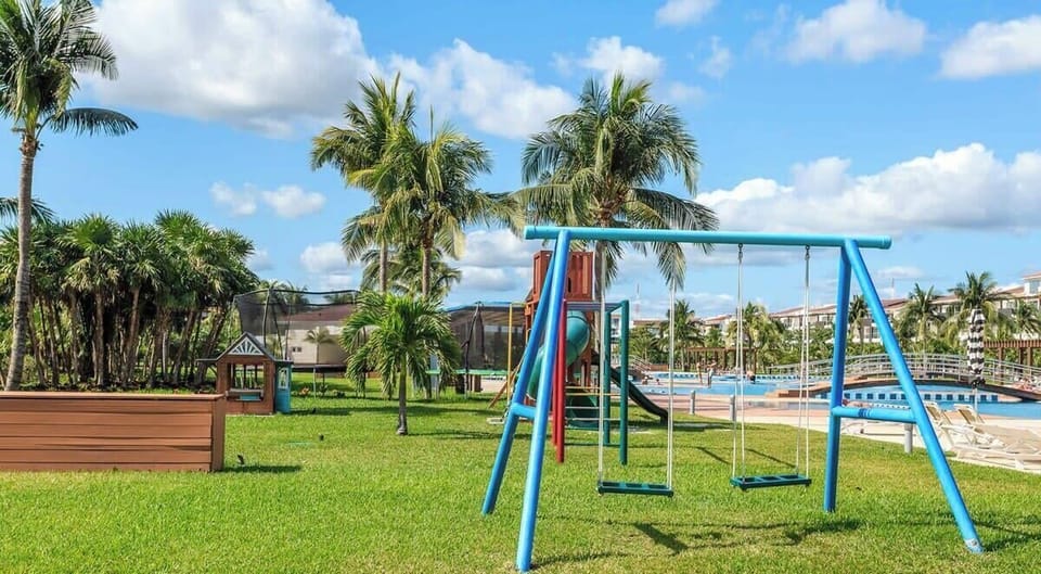 Outdoor playground with swings and slides set in a tropical garden near the pool area.