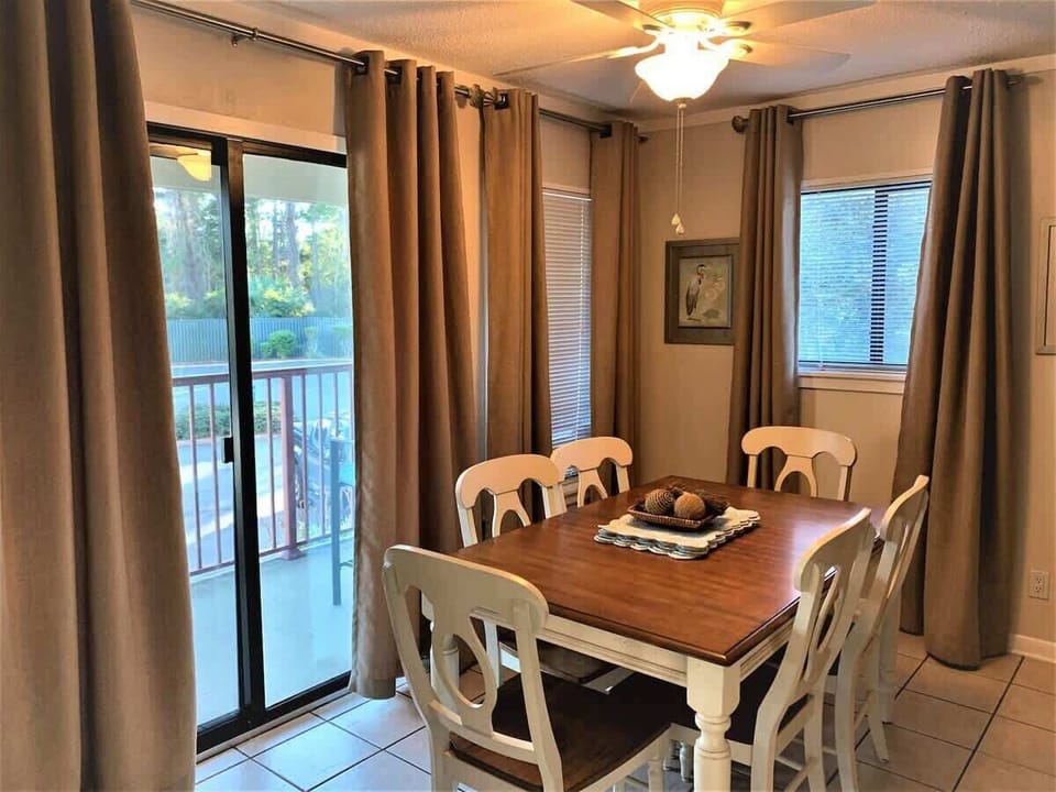 A dining table with seating for six, framed by floor-to-ceiling neutral curtains.