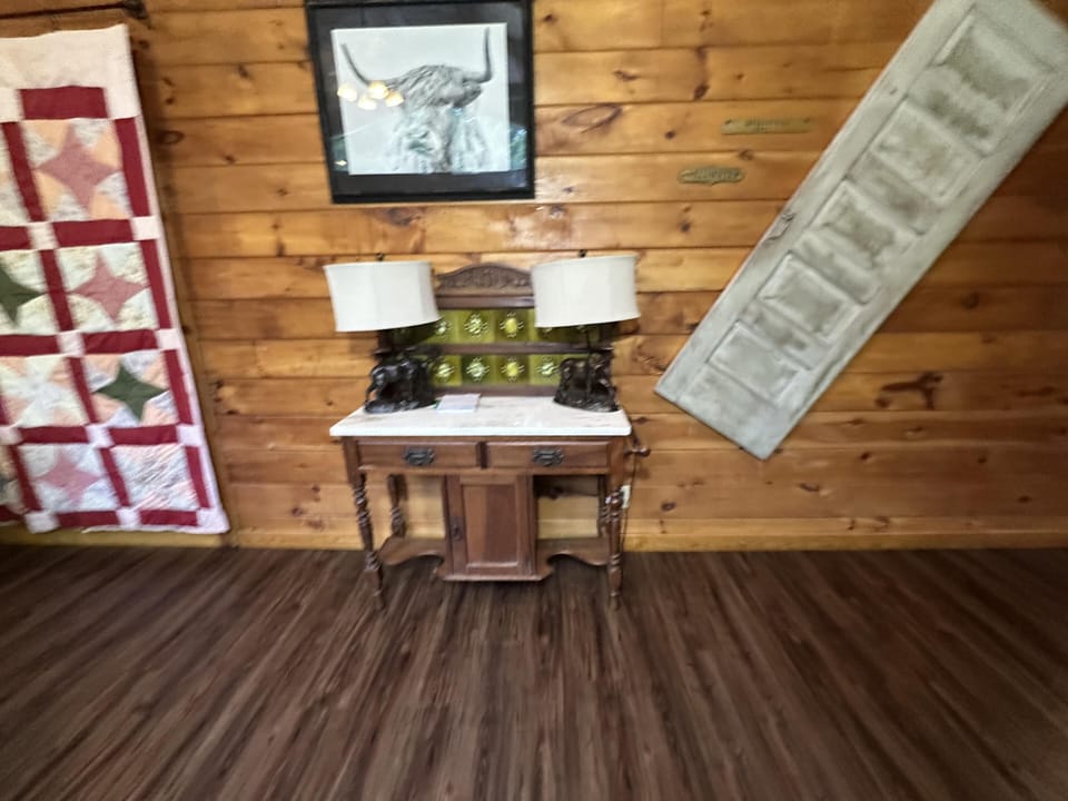 Wood-paneled wall features an antique wooden side table with marble top, twin lamps, and framed animal print.