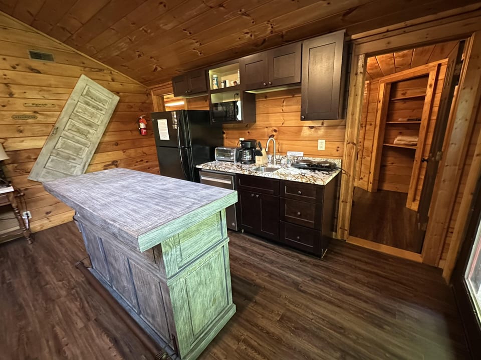 Kitchen area with dark wood cabinets, granite countertop, black appliances, and a distressed green island.
