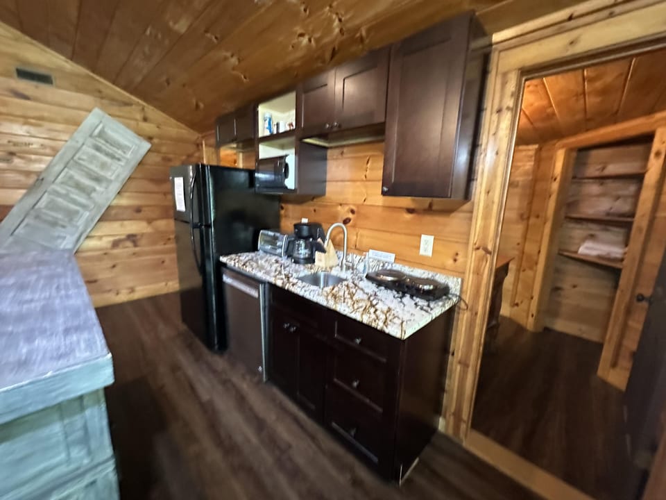 Kitchen with dark wood cabinets, granite countertop, black refrigerator, coffee maker, and wood-paneled walls.