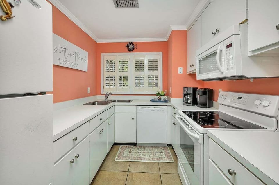 Kitchen with white cabinets, coral walls, and white appliances