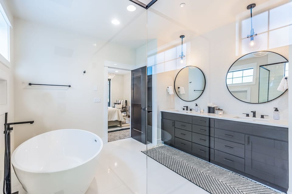 Master Suite En Suite Bathroom Located on the Main Floor - Modern dual-sink bath with custom cabinetry, soaking tub and glass door