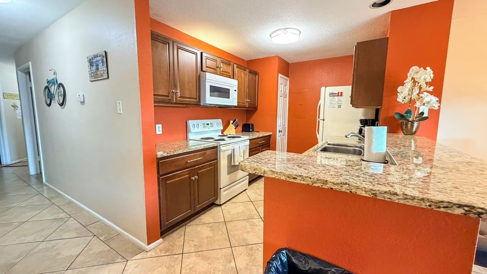 Cook your favorite meals in this fully equipped kitchen with granite counters, stainless appliances, and warm orange accents.