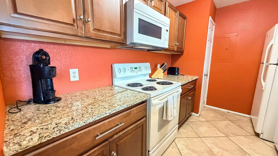 Your fully equipped kitchen features granite counters, modern appliances, and warm orange walls that create a cheerful space for preparing meals.
