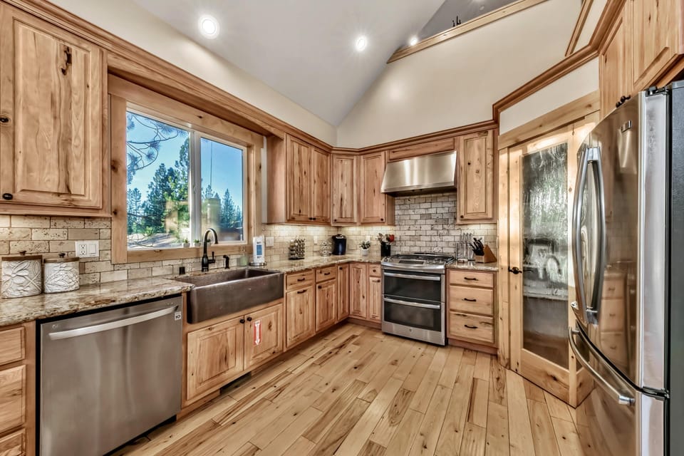 Kitchen with knotty pine cabinetry, stainless steel appliances, brick-pattern backsplash, and a hammered metal farmhouse sink beneath a window.