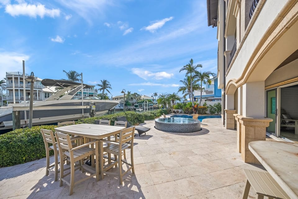 Waterfront patio with outdoor dining and pool, surrounded by tropical palms and marina views.