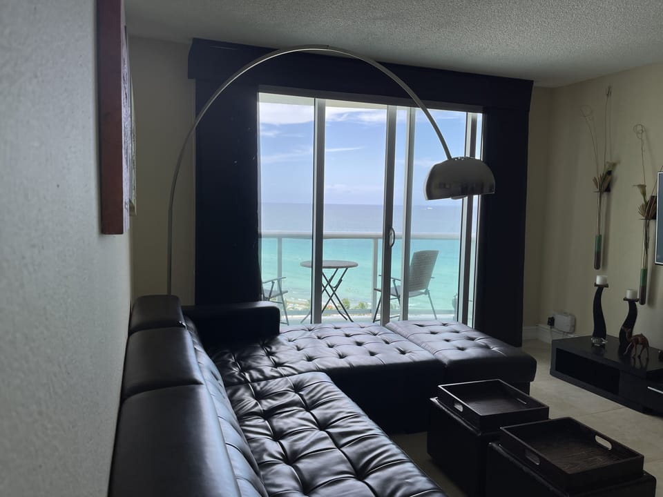 Ocean view Living room w/Flat smart TV, sofa bed, and blackout shades.