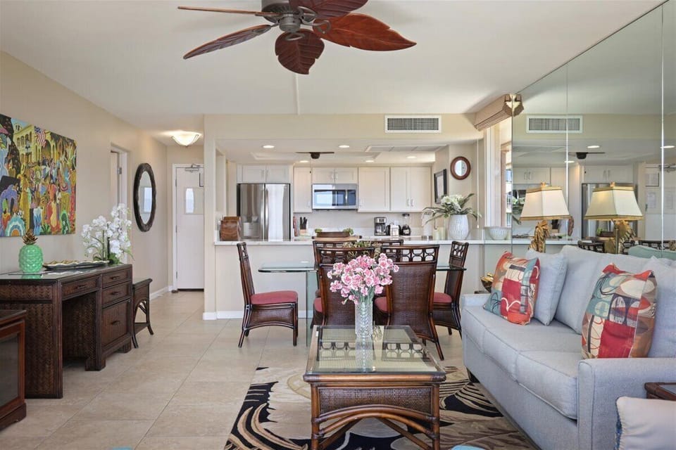 Relax in your bright, inviting living space with vibrant artwork, comfortable seating, and a fully equipped kitchen where you can prepare your favorite meals. The tropical ceiling fan and colorful accents create a welcoming retreat.
