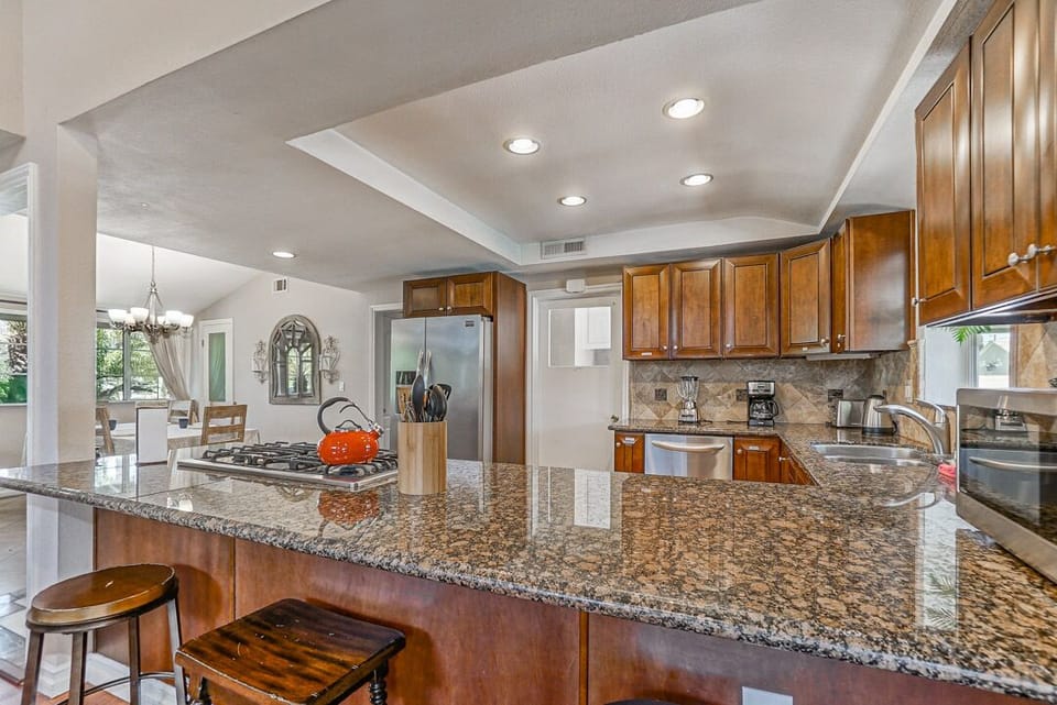 - Granite kitchen island with bar stools for casual dining   - Stainless appliances and wood cabinetry add modern touch   - Open design makes cooking and hosting simple and fun