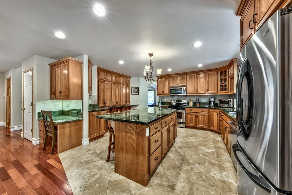 Kitchen features honey-toned cabinets, green granite countertops, stainless steel appliances, and a central island with stools.