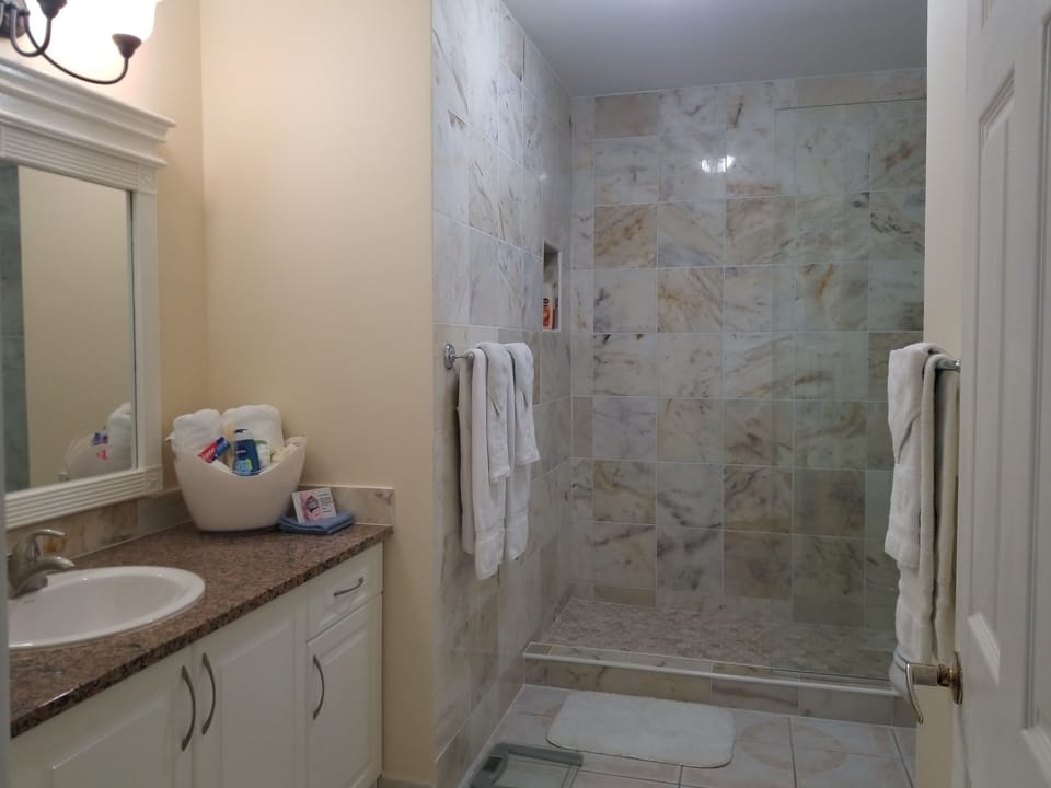 Spacious Bathroom With Glass Shower Stall, Marble Tiles & Hand Sprayer.