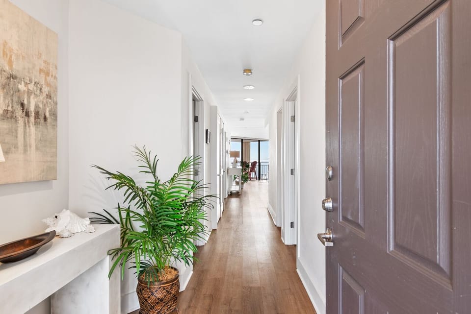 Step into your bright hallway with warm wood floors, natural light, and tropical plants creating a welcoming atmosphere.