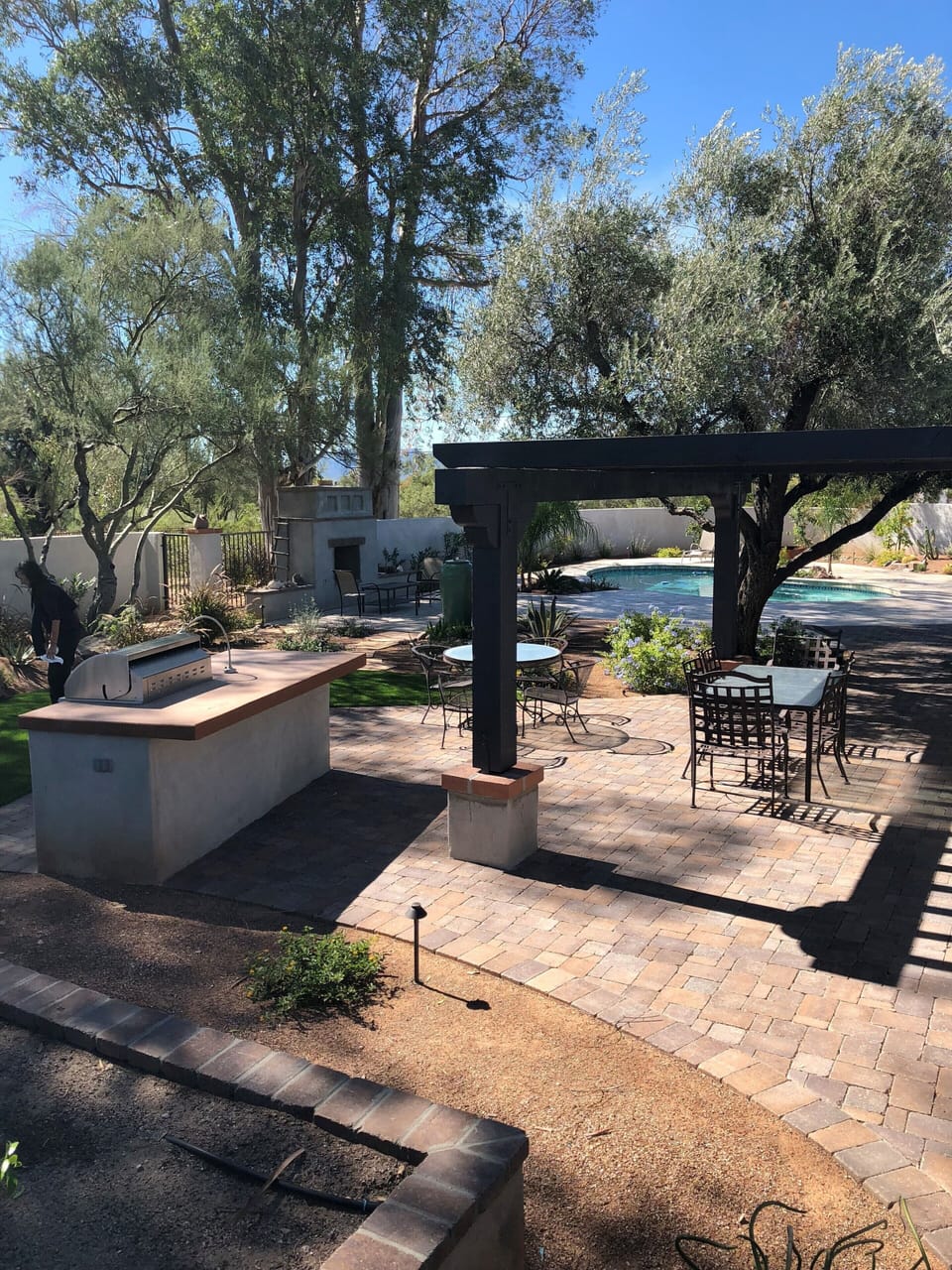 Outdoor dining under wooden pergola and olive tree near bar and grill 
