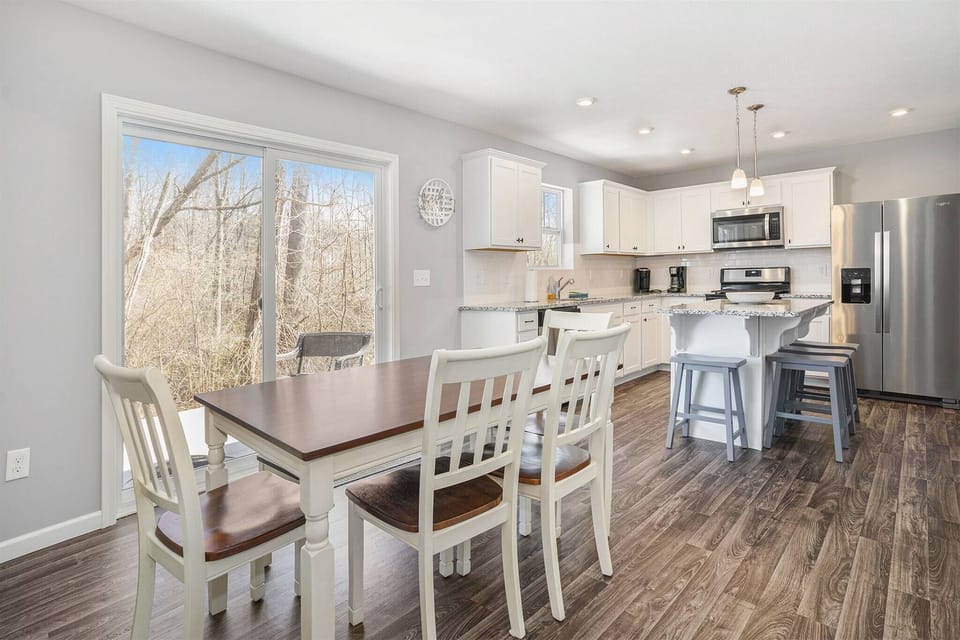 Bright dining room area with wooded views and an open layout flowing into a modern, fully equipped kitchen.