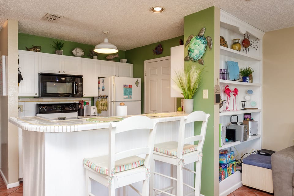Your bright kitchen features cheerful green accents, white cabinetry, and a breakfast bar where you can enjoy morning coffee together.