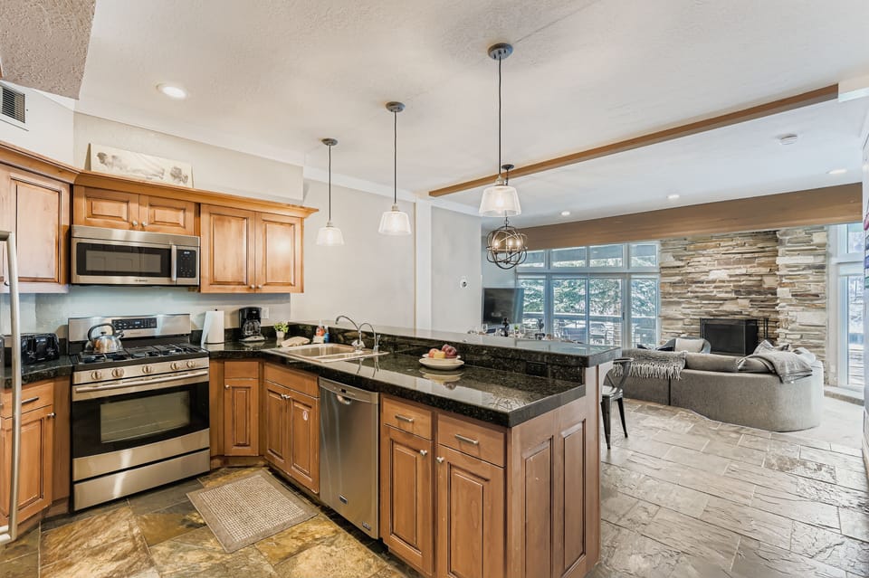 A bright, open kitchen awaits with granite counters, stainless appliances, and everything you need to whip up meals. Beyond, your living space flows seamlessly with cozy seating and mountain views through expansive windows.