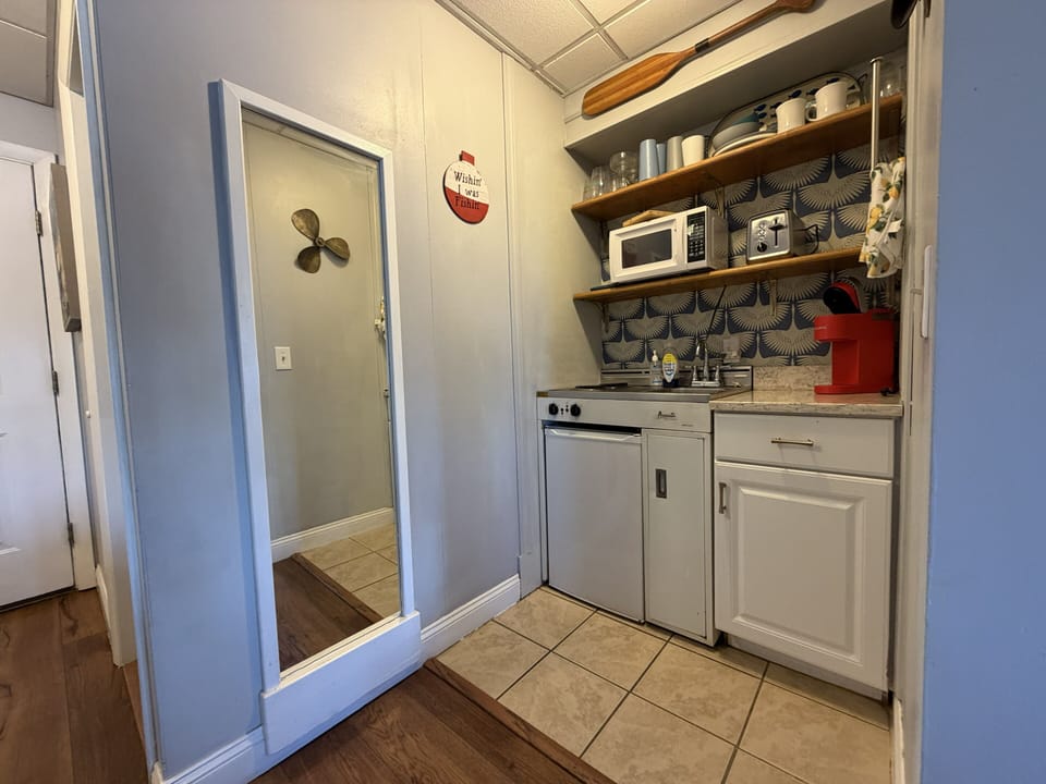 Your cozy kitchenette features a microwave, stove, and mini fridge—perfect for quick meals or coffee mornings. Open shelving keeps essentials within reach while charming backsplash tile adds warmth.