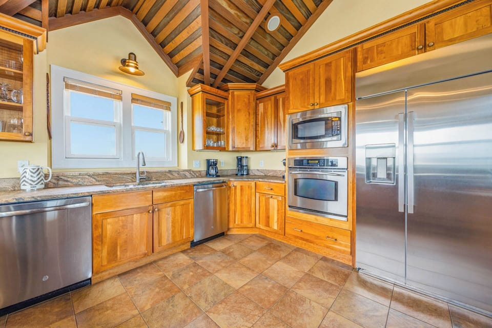 Your vacation kitchen showcases stunning vaulted wood-beam ceilings, gleaming stainless-steel appliances, and granite counters—fully equipped for crafting memorable meals with ocean views through bright windows.