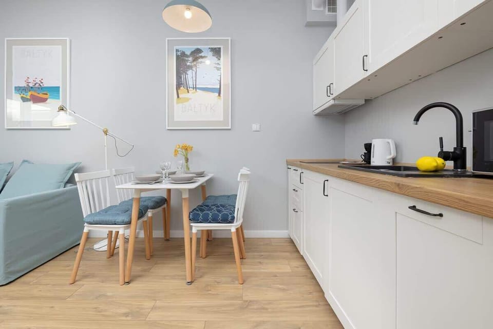 A compact dining area adjacent to a modern white kitchen, with soft wooden floors and minimalist decor.