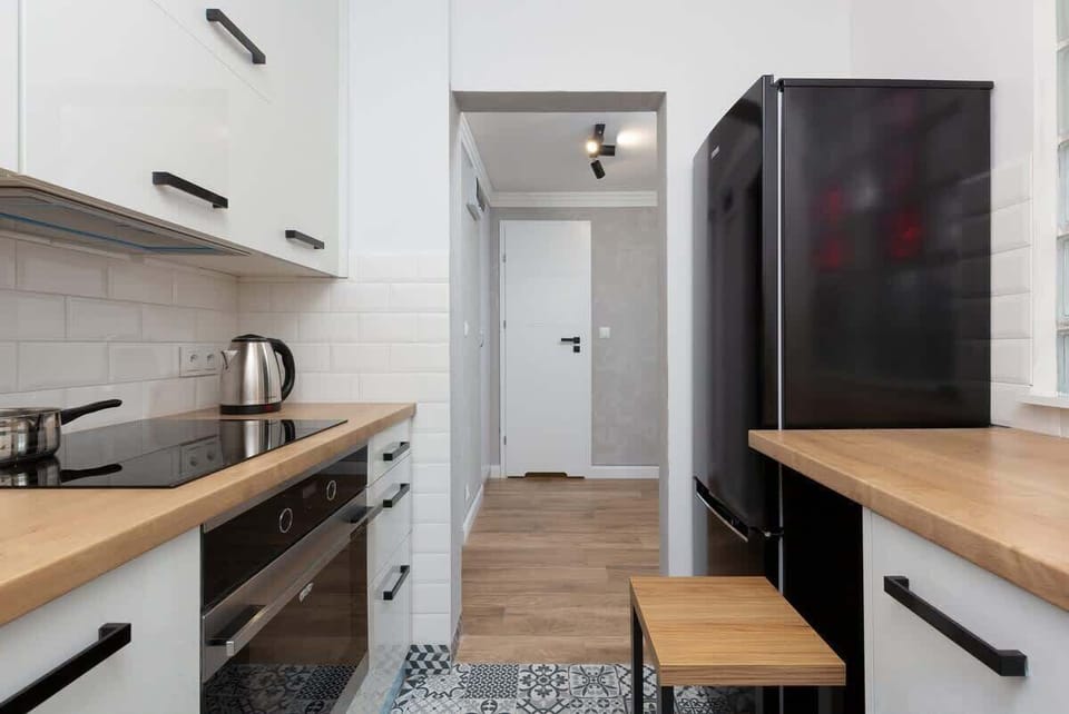 A compact kitchen with white cabinets, wooden countertops, and sleek black appliances.