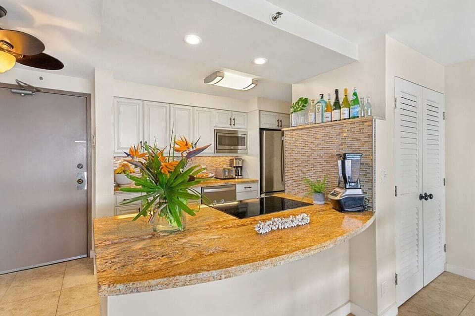 Kitchen with granite countertop and floral centerpiece, stainless appliances and mosaic backsplash adding polish.