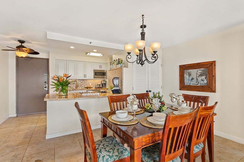 Alternate view of dining with kitchen beyond, white cabinetry and granite counters framed by chandelier light.