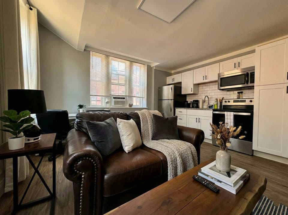 Open living and kitchen area with leather sofa, desk chair, and white kitchen cabinetry.