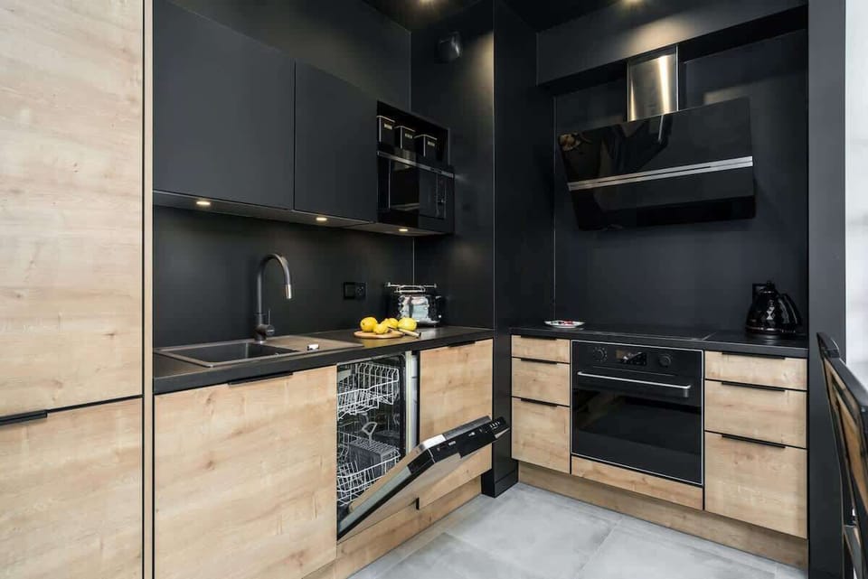 A sleek kitchen featuring black walls, light wooden cabinets, and modern appliances.