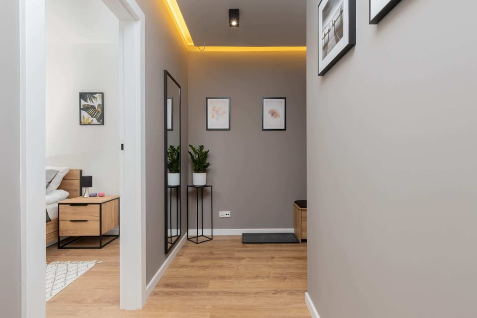 Spacious hallway with soft lighting, wooden flooring, and wall frames that create a welcoming entrance.Kom