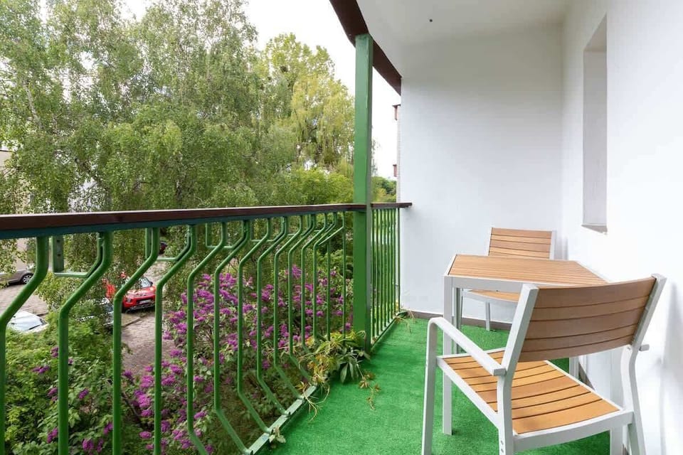 An outdoor seating area with wooden chairs and a table, overlooking a lush green garden or courtyard.