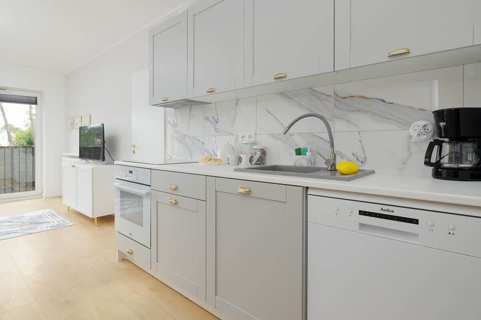 A modern kitchenette with white cabinets, marble-patterned countertops, and essential appliances, offering a clean and functional cooking area.