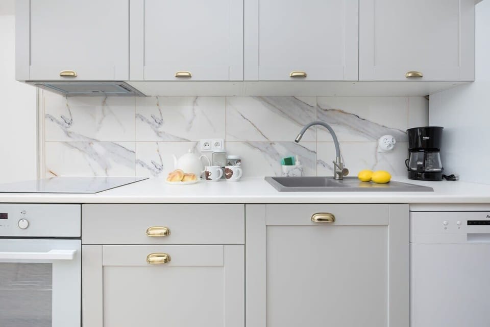 A close look at the kitchenette with clean, minimalist design featuring white cabinetry, a tiled backsplash, and compact appliances.