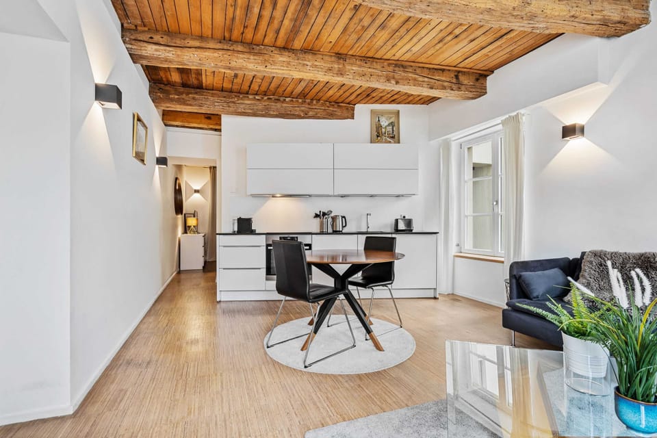 Open-concept living area with a dining table and fully equipped kitchen, featuring rustic wooden beams.